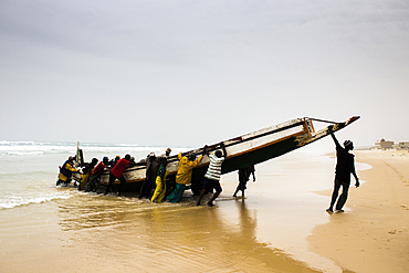 Men unload a fish canoe in the afternoon fish market in Mboro Plage beach when the canoes arrive loaded