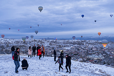 Cappadocia in winter covered with snow, tourists and hot-air balloon taking off near G√∂reme