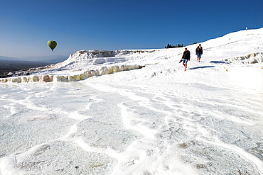 Travertine terrace formations at Pamukkale, tourists and hot-air balloon