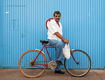 Man on bicycle in front of blue wall, Tonal·, Mexico.