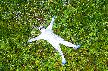 Person with a safety suit lying down in a flowers carpet in a forest area. Ayegui, Navarre, Spain, Europe