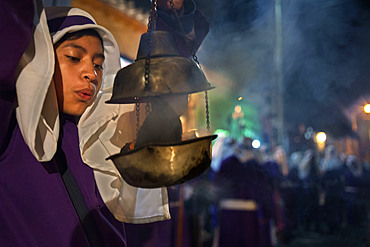 A boy spreads incense at the Jesus Nazareno del Perdon procession during Easter Holy Week in Antigua Guatemala. Holy Week (Semana Santa) carpet of colored sawdust (alfombras) being prepared on Antigua street. Jesus Nazareno de la Penitencia Procession in Antigua, Guatemala.