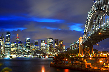 Side view of Sydney Harbour bridge architectural landmark and city at sunset. Illuminated arch of the bridge reflecting in blurred waters Sydney, New South Wales, Australia