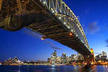 Side view of Sydney Harbour bridge Opera House and city CBD at sunset. Illuminated arch of the bridge reflecting in blurred waters Sydney, New South Wales, Australia