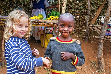 European blonde girl giving the hand and sharing with a black children boy in the primary and second school in a small village near Kitui city in the Kamba country in Kenya, Africa.