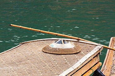 A covered tour boat docked on the Tuojiang River in Fenghuang, China, with a traditional conical hat on top.