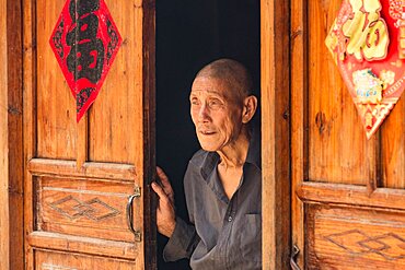 An elderly Chinese man looks out the doorway of his traditional house the Yao village of Huangluo, China.