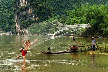 A cormorant fisherman in a conical hat throws a cast net in the Li River, Xingping, China.