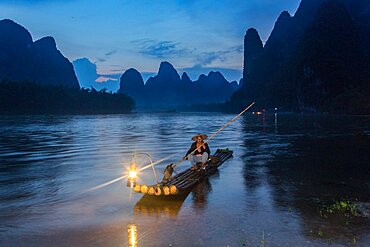 A traditional cormorant fisherman on a bamboo raft with his cormorants on the Li River, Xingping, China.