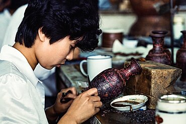 An artisan attaches cloisons or wire strip to make the design for a cloissone vase in a workshop in Beijing, China.