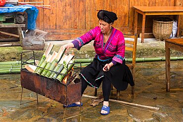 A Red Yao woman cooking rice in bamboo tubes over an open fire in Jinking, Longshen, China.