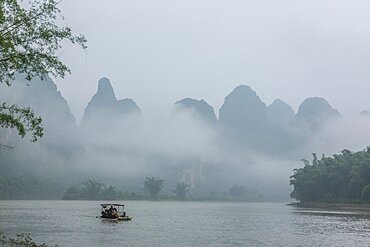 A small tourist boat on a foggy morning on the Li River near Yangshou, China.