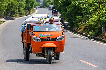 A Chinese man hauling good in an open three-wheeled utility truck in rural Hunan Province, China.