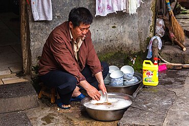 A man washed dishes by hand in a bowl outside a restaurant in the ancient town of Furong, China.