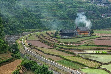 Smoke rises from a farm house surrounded by terraced rice paddies in rural Hunan Province, China.