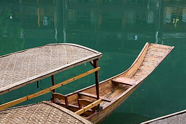 A covered tour boat docked on the bank of the Tuojiang River in Fenghuang, China.