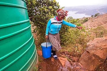 Woman carrying a bucket over rocky terrain in the Hhohho region of Swaziland, Africa.