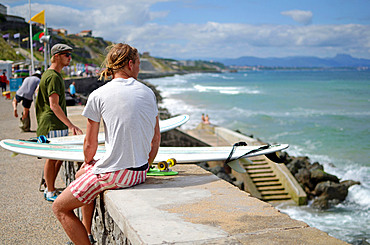 Surfers watch waves in Cote des Basques beach at sunset, Biarritz