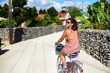 Young woman rides bike in Taketomi Island, Okinawa Prefecture, Japan