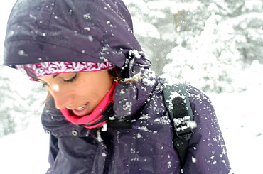 Young woman faces blizzard while hiking in snowy day at Pe?alara, highest mountain peak in the mountain range of Guadarrama, Spain