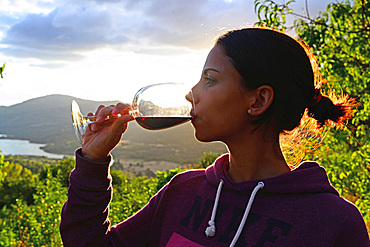 Young woman drinks wine at sunset in valley