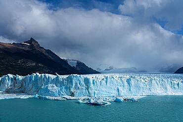 The jagged face of Perito Moreno Glacier and Lago Argentino in Los Glaciares National Park near El Calafate, Argentina.  A UNESCO World Heritage Site in the Patagonia region of South America.  Icebergs from calving ice from the glacier float in the lake.  Behind at left is Cerro Moreno.