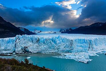 The jagged face of Perito Moreno Glacier and Lago Argentino in Los Glaciares National Park near El Calafate, Argentina.  A UNESCO World Heritage Site in the Patagonia region of South America.  Icebergs from calving ice from the glacier float in the lake.  In the distance at left is Cerro Gardener.