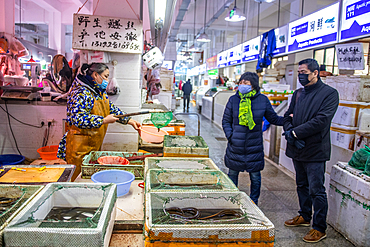 Shanghai, China, 26th Jan 2020, Woman store vendor wearing masks shows living eel to couple wearing masks at seafood market