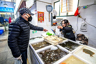 Shanghai, China, 26th Jan 2020, A man wearing a mask exchanges money with woman store merchant for seafood at market