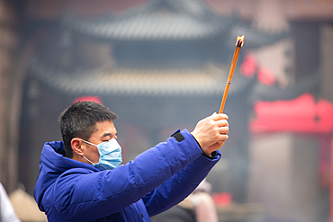 Shanghai, China, 23rd Jan 2020, A man wearing a mask prays with burning joss sticks