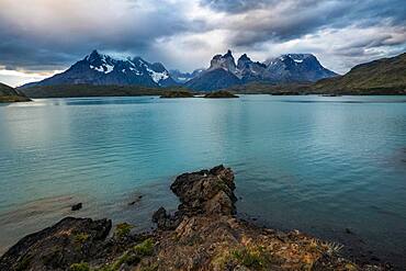 The rocky shoreline of Lago Pehoe in Torres del Paine National Park, a UNESCO World Biosphere Reserve in Chile in the Patagonia region of South America. Across the lake is the Paine Massif in the low clouds.