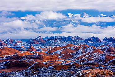 Snow on the Petrified Dunes in winter with the La Sal Mountains in the clouds behind. Arches National Park, Moab, Utah.