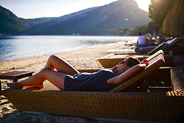 Young caucasian woman speaking on the phone while laying on beach chair during holidays