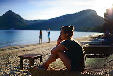 Young caucasian woman speaking on the phone while sitting on beach chair during holidays