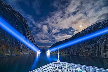 Exiting the narrow Trollfjord by searchlight and under moonlight, on the northbound voyage of the Hurtigruten ferry ship the ms Trollfjord, on October 15, 2019. Capella is at top; Betelgeuse and Orion are rising at centre at the mouth of the fjord; Aldebaran is partly in cloud left of the Moon.