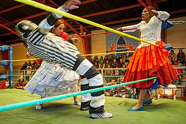 Lucha Libre. Combat between Dina with orange skirt and Benita la Intocable , cholitas females wrestlers ,with referee in the middle, Sports center La Ceja, El Alto, La Paz, Bolivia