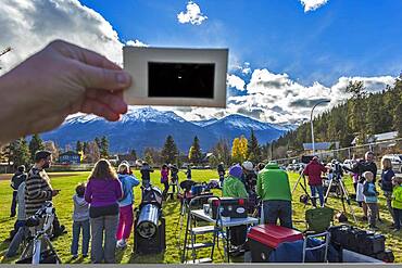 The partial solar eclipse of October 23, 2014 as seen from Jasper, Alberta, at a public event in Centennial Park as part of the annual Dark Sky Festival. This is a single-exposure image showing the scene near mid-eclipse with telescopes from volunteers from the Royal Astronomical Society of Canada, and the mostly clear skies above with the crescent Sun visible through the handheld polymer solar filter.