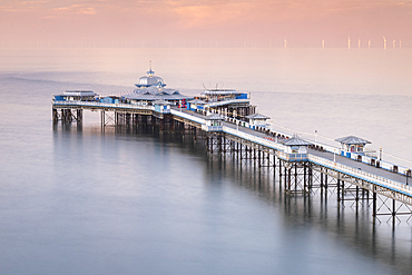 Llandudno Pier and the distant Wind Turbines of the Gwynt y Mor Offshore Wind Farm at sunset, Llandudno, Conwy County Borough, North Wales, UK