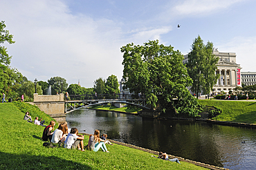 Young people on the bank of the Canal surrounding the Old Town of Riga, in front of the National Opera House, Riga, Latvia, Baltic region, Europe