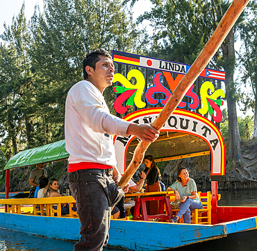 Trajinero punting barge at popular tourist attraction, people boating on colourful barges on canal at Xochimiloco, Mexico City, Mexico, North America