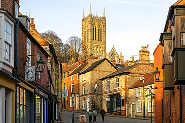 People walking up Steep Hill in evening light, cathedral tower rising above buildings, Lincoln, Lincolnshire, England, UK