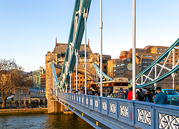 People and open top tour buses cross Tower Bridge in late afternoon, London, England, UK