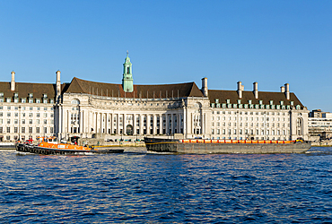 Barge boat passing County Hall on south bank of River Thames, Lambeth, London, England, UK completed 1922