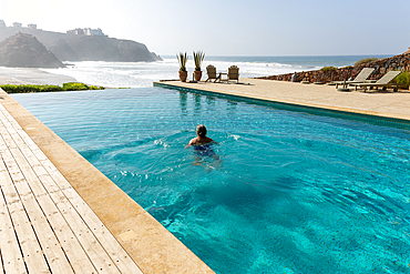 Woman swimming in infinity pool by Atlantic Ocean, Hotel Auberge Dar Najmat, Mirleft, Morocco, North Africa, Africa