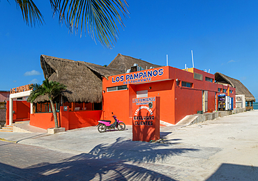 Thatched palapa roofed buildings and bright orange exterior of Los Pampanos seaside restaurant, Celestun, Yucatan, Mexico, North America