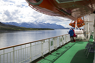 Two people on deck viewing scenery on Hurtigruten ferry ship, near the Arctic Circle crossing, Norway, Scandinavia, Europe