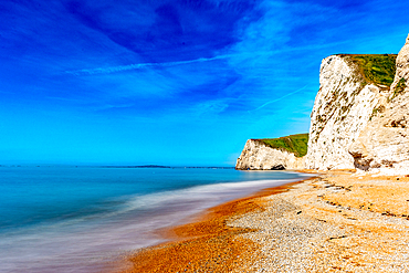 Serene beach with smooth water effect, blue skies, and towering cliffs on a sunny day at Durdle Door, Jurassic Coast, UNESCO World Heritage Site, Dorset, England, United Kingdom, Europe