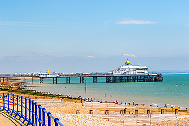 Sunny seaside landscape with pier extending into the sea, blue railings in the foreground, and clear blue sky, Eastbourne, East Sussex, England, United Kingdom, Europe