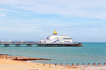 Serene beachscape with a classic pier extending into calm waters under a cloudy sky, with wooden groynes in the foreground, Eastbourne, Easts Sussex, England, United Kingdom, Europe