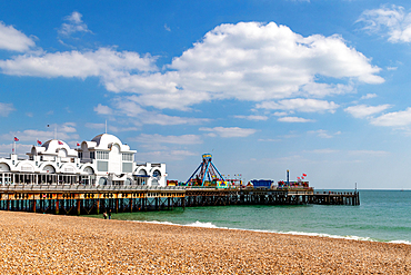 Sunny beach with pebbles and a traditional pier with amusement attractions extending into the sea under a clear blue sky, Eastbourne, East Sussex, England, United Kingdom, Europe